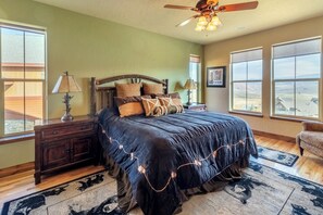 A bedroom with a large bed, a wooden headboard, a ceiling fan, and a view of the landscape through the windows. - Beautiful 4-bedroom house in Granby perfect for your getaway (Granby)