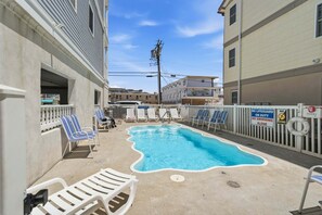 Une piscine entourée de bâtiments, avec des chaises longues et un poste de surveillance pour les sauveteurs.