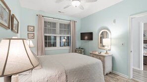 Une chambre à coucher comprenant un lit, une lampe de chevet, une commode, un téléviseur et un ventilateur de plafond.