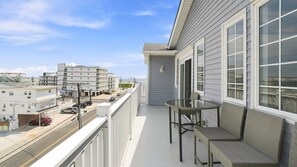 Un balcon avec une table et des chaises, donnant sur une rue bordée d’immeubles et offrant une vue sur un ciel dégagé.