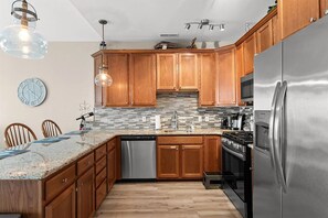 Eine moderne Küche mit Holzschränken, Edelstahlgeräten, einer Arbeitsplatte aus Granit und einem Essbereich mit Stühlen.