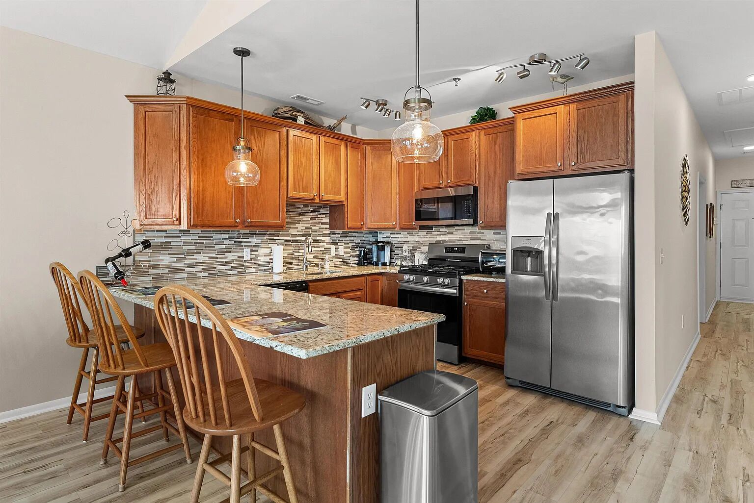A modern kitchen with wooden cabinets, a stainless steel refrigerator, and a granite countertop.