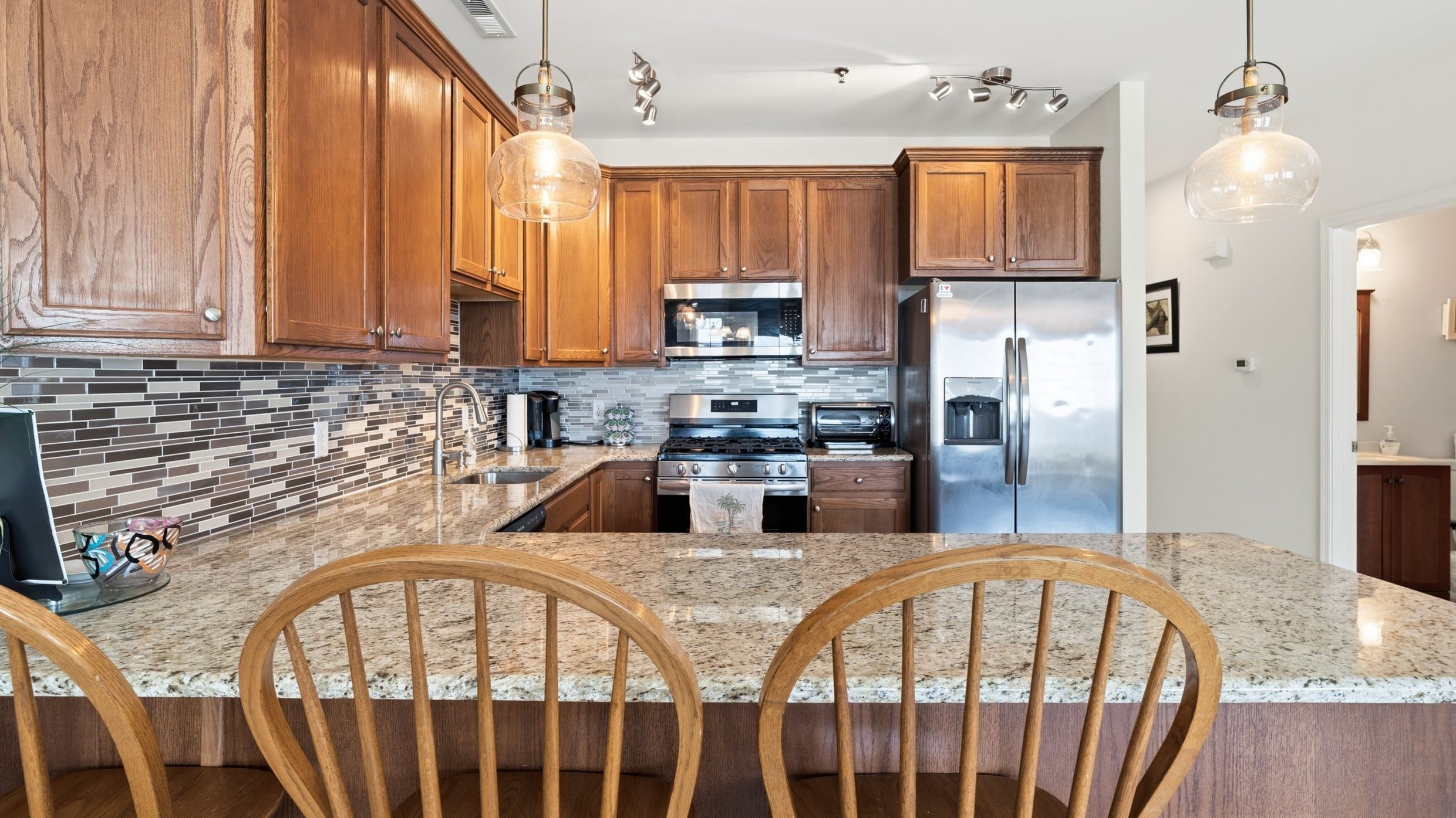 A kitchen with wooden cabinets, a granite countertop, stainless steel appliances, and pendant lighting.
