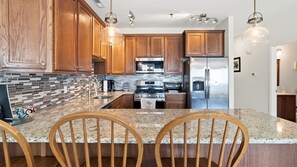 A kitchen with wooden cabinets, a granite countertop, stainless steel appliances, and pendant lighting. - Top-Floor Coastal Condo with Pool, Private Deck & Walk to the Beach (Wildwood Crest)
