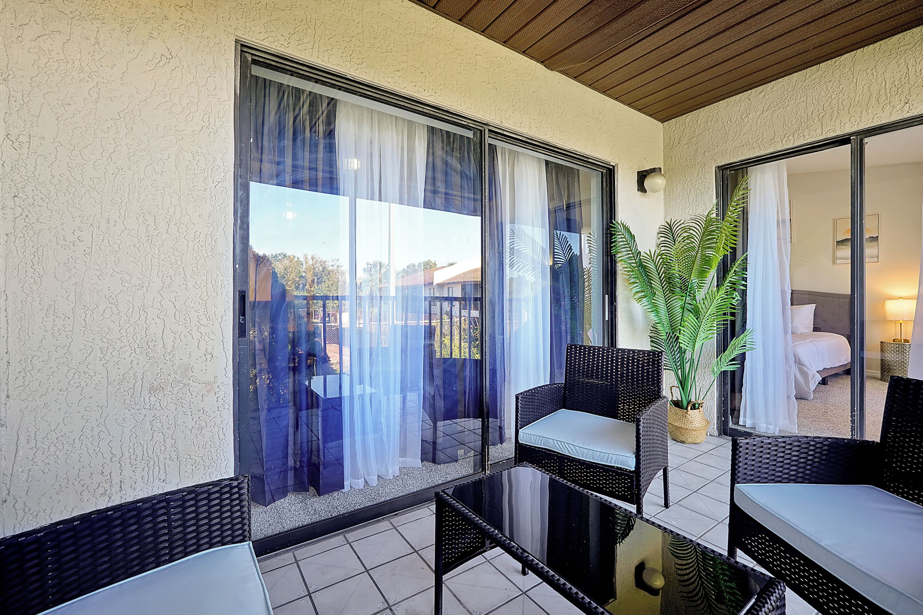 A balcony with wicker furniture, a potted plant, and a view of a building.