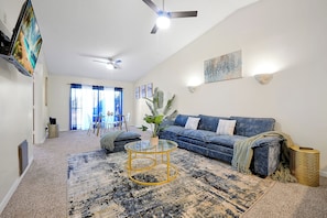 Ein Wohnzimmer mit einem blauen Sofa, einem Glastisch und einem Deckenventilator.