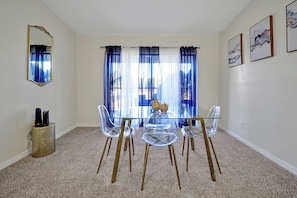 A dining area with a glass table and chairs, a mirror, and curtains.