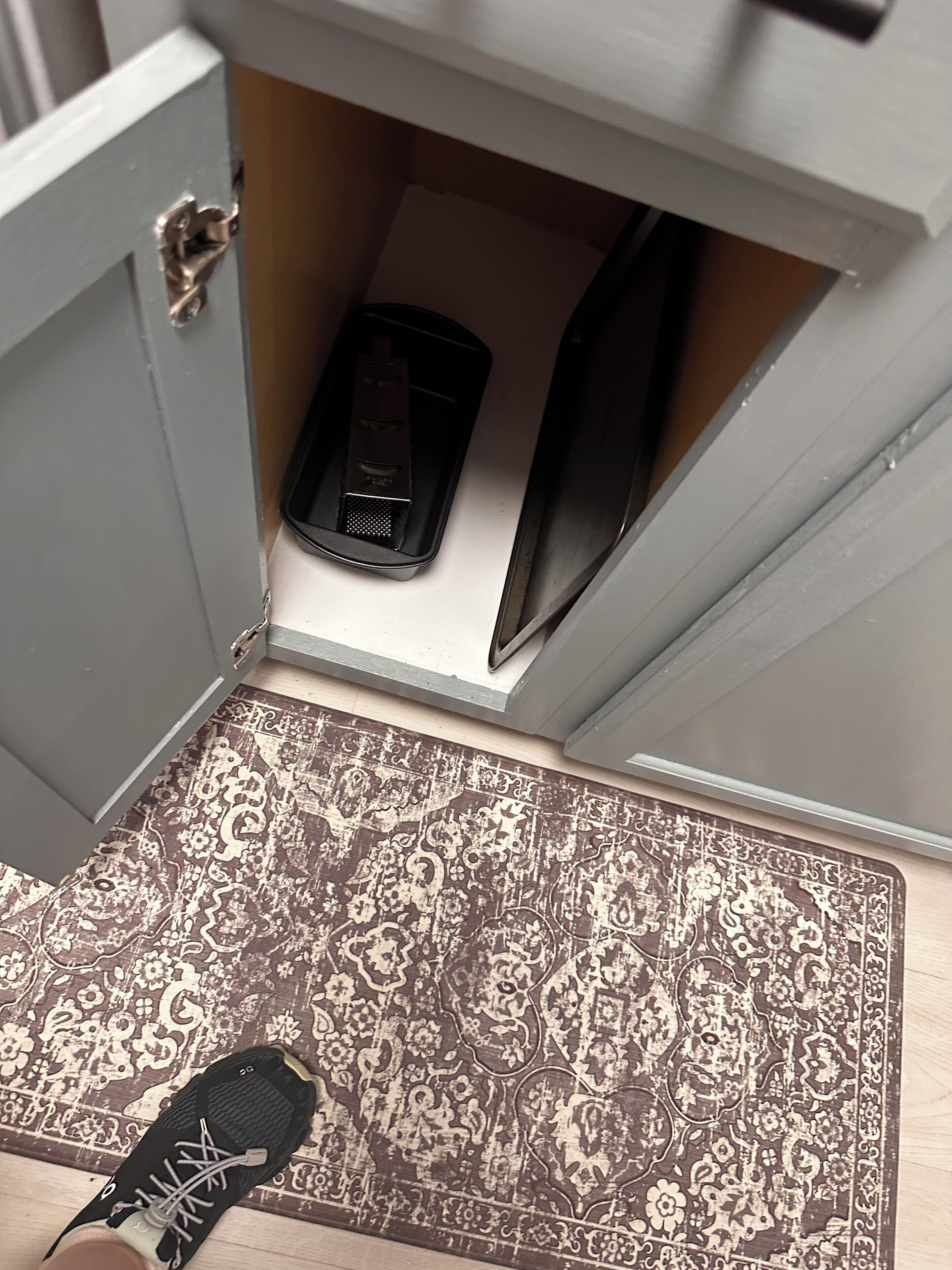 A shoe on a patterned rug, a door with a latch, and a black object inside a cabinet.