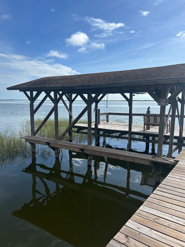 A wooden pier extending into calm water with a covered seating area and a warning sign about alligators.