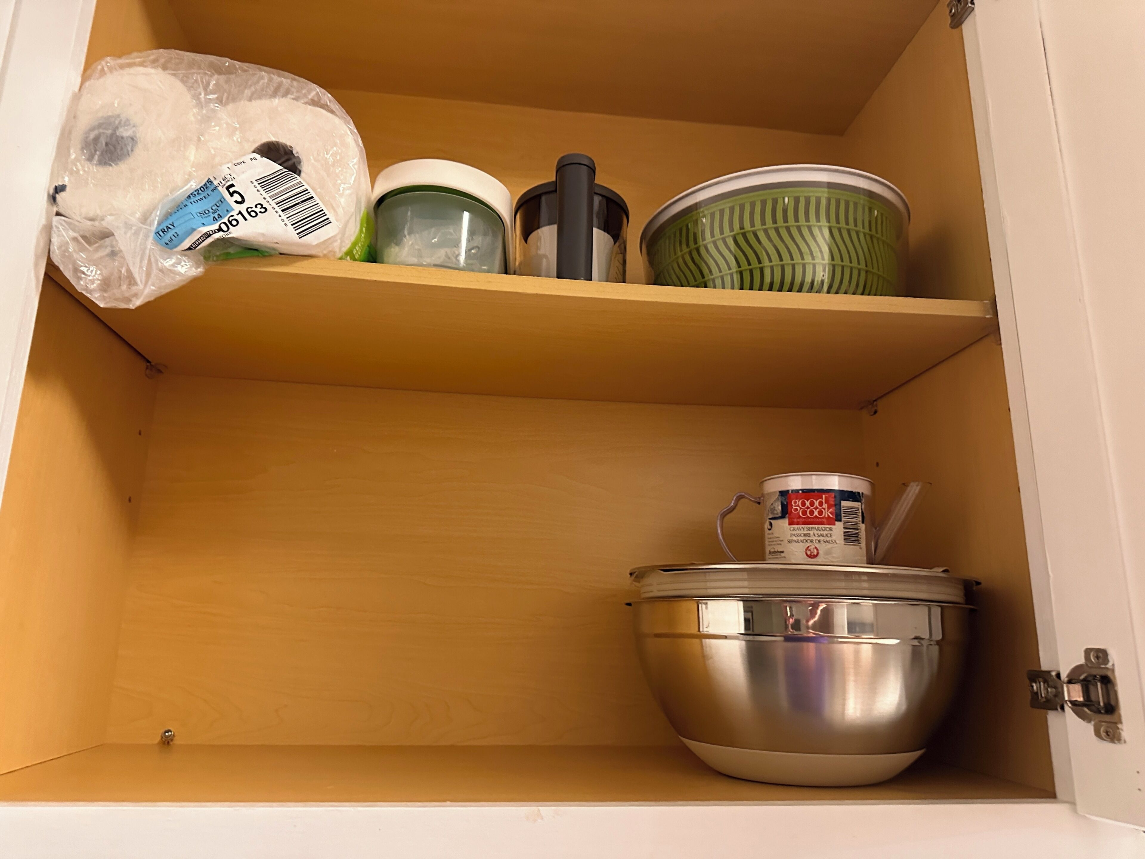 A kitchen cabinet with a shelf containing a plastic bag, a green container, a black container, and a canister.