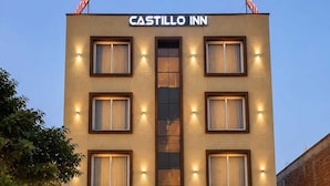 Un hotel llamado CASTILLO INN con una fachada moderna, múltiples ventanas y una entrada central con escalones que llevan a la puerta.
