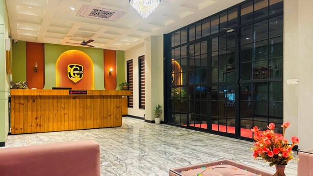 A hotel reception area with a wooden reception desk, a reception sign, a chandelier, a large window, and a red carpet. - Hotel Castillo Inn (Jaipur)