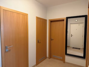 A hallway with three wooden doors, one with a vent, and a large mirror on the wall.