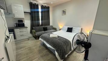 Un dormitorio con cama, mesita de noche, lámpara y un ventilador de pie.
