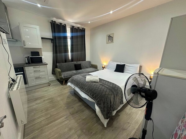 Un dormitorio con cama, mesita de noche, lámpara y un ventilador de pie.