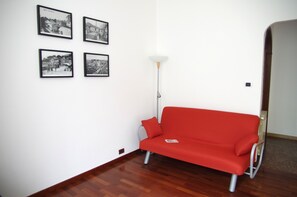 A room with a red sofa, a floor lamp, and four black-and-white photographs on the wall.