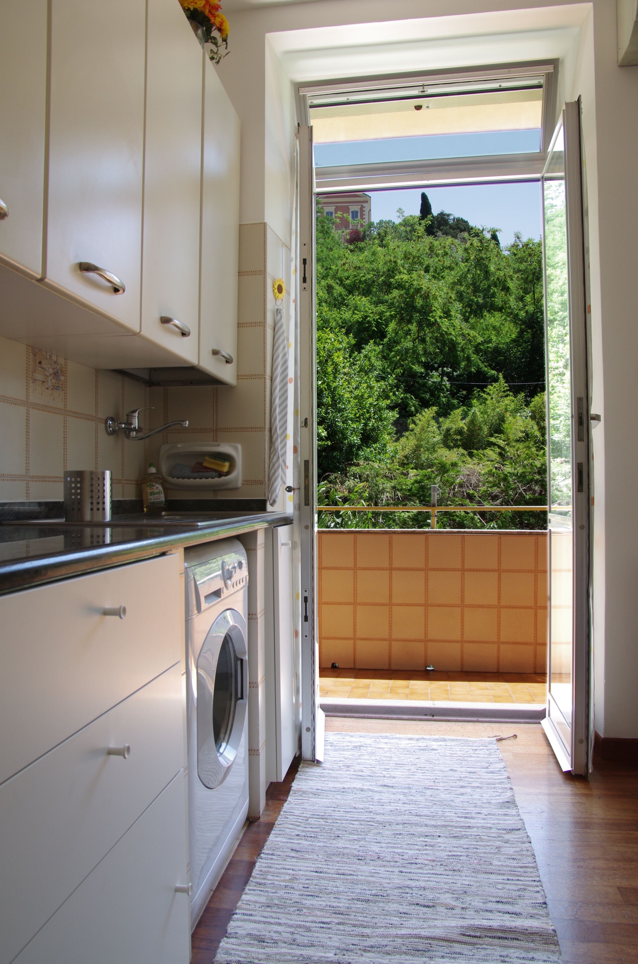 Eine Küche mit Waschmaschine, Spüle und Fenster zum Balkon mit Blick auf Grünflächen.