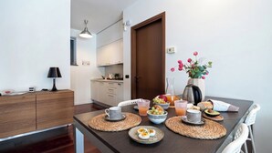 A modern kitchen with a dining table set for breakfast, including eggs, fruit, and beverages. - Italianway Comfort - Vico Magistretti 1 B (Milano)