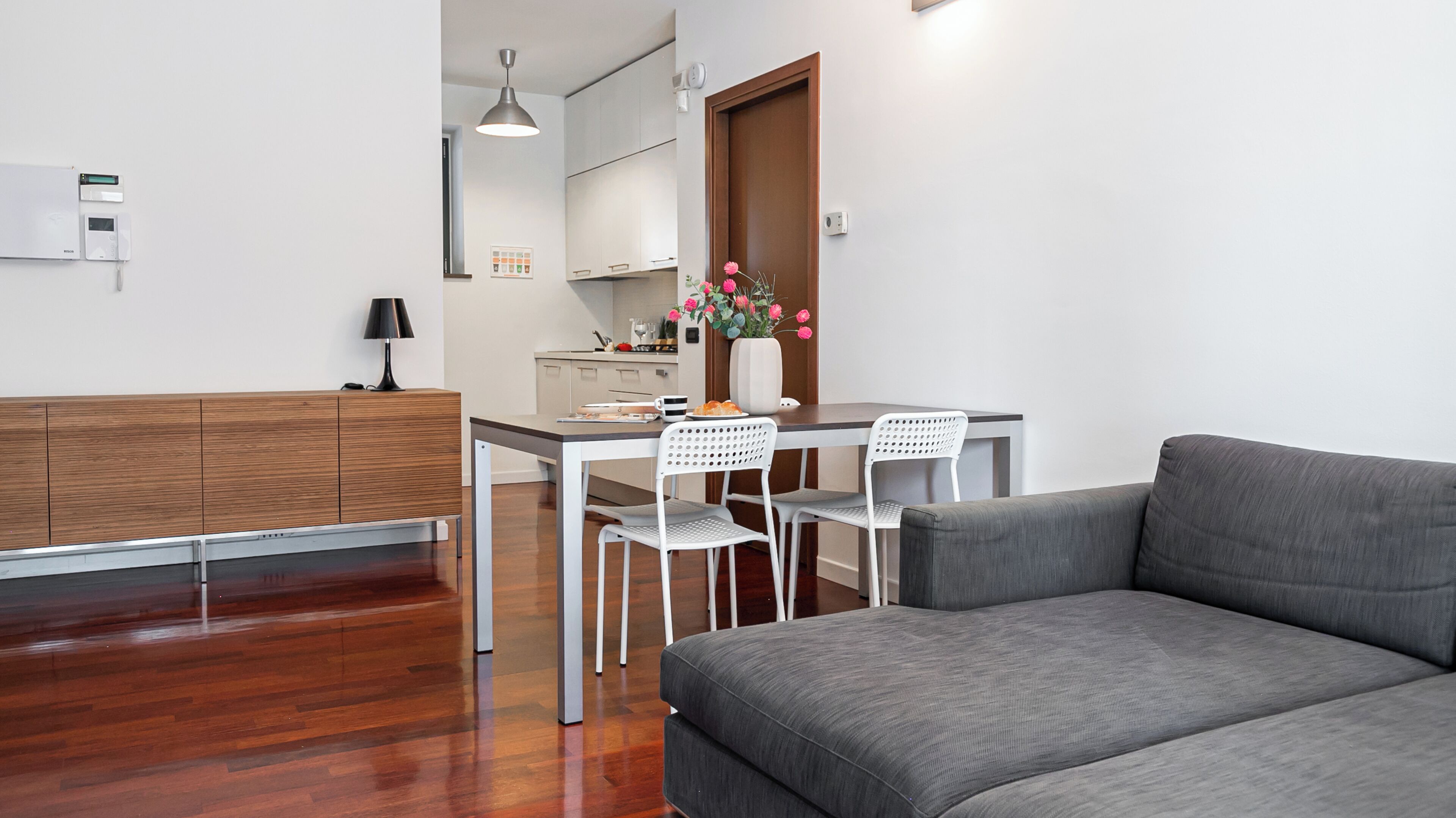 Una sala de estar moderna con un sofá gris, una mesa de comedor con dos sillas y un mueble de madera.