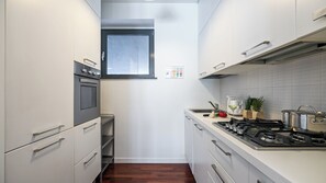 Eine kompakte Küche mit weißen Schränken, einem Einbauofen, einem Gasherd und einem Fenster über der Spüle.