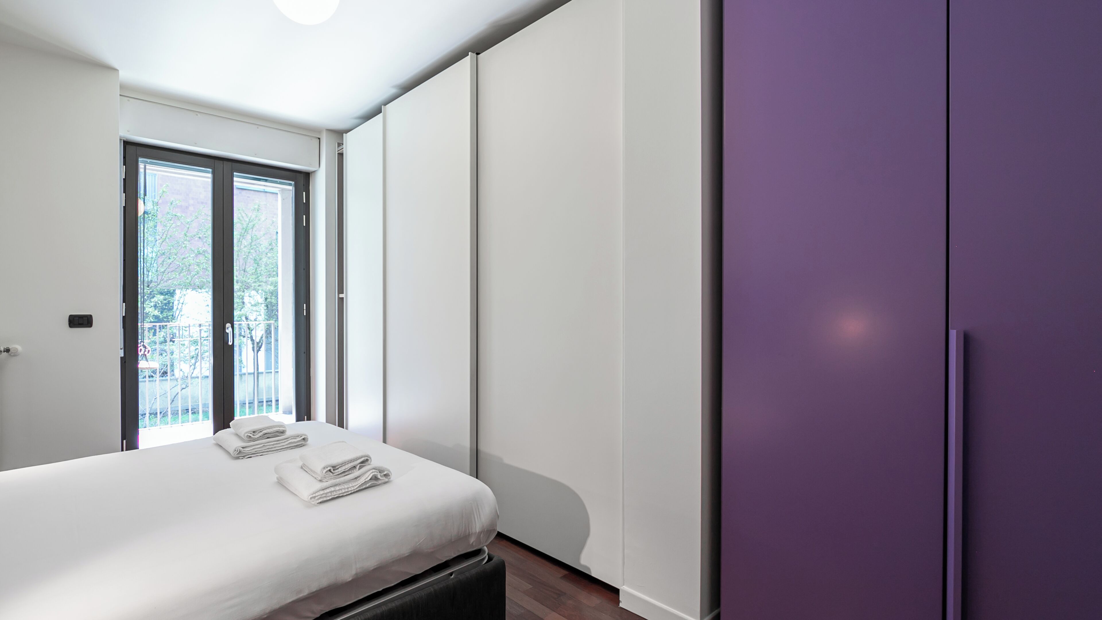 Un dormitorio con cama, armario y puerta corredera a un balcón.