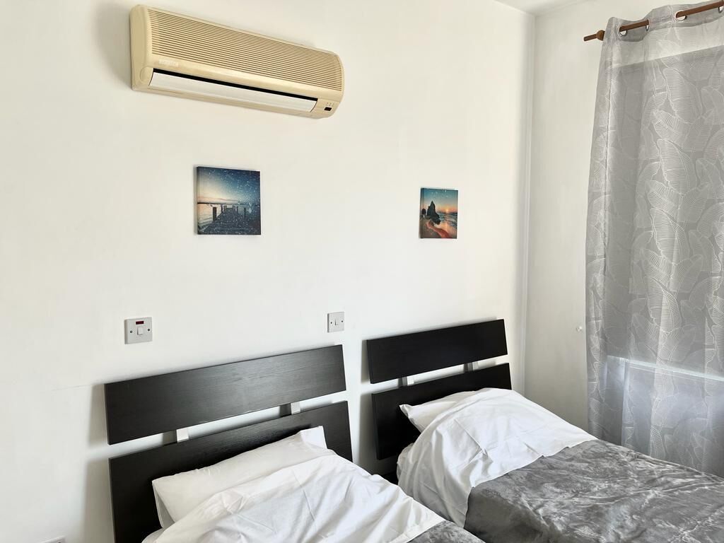 A bedroom with two beds, an air conditioner, and two wall-mounted pictures.