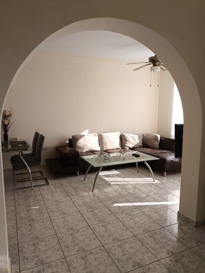 A living room with a glass coffee table, a brown leather sofa, a glass dining table, and a ceiling fan. - MOLOS Complex  (Pafos)