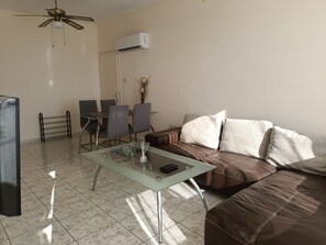 Una sala de estar con una mesa de centro de vidrio, sofá de cuero marrón y un comedor con sillas y una mesa.