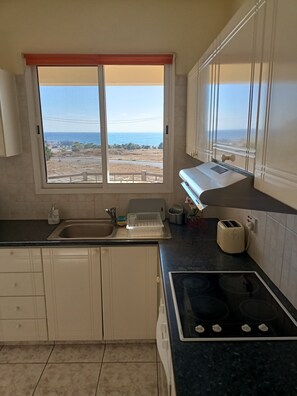 A kitchen with a window view, a sink, a stove, and cabinets. - MOLOS Complex  (Pafos)