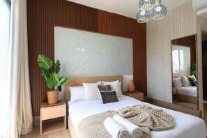 Ein Hotelzimmer mit einem großen Bett, einem Blumentopf, einem Spiegel und einer modernen Deckenleuchte.