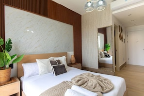 A modern hotel room with a large bed, a wooden headboard, a marble wall, a mirror, and a potted plant. - Suite fourth floor pool view Downtown Punta Cana (Punta Cana)