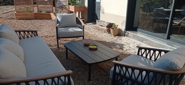 An outdoor seating area with a sofa, chairs, and a table, surrounded by gravel and wooden planters.