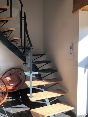 A spiral staircase with wooden steps and metal railings, a round wicker chair with a cushion, and a wall-mounted light fixture.