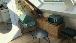 A compact living space with a skylight, a teal chair, a small table, a microwave, and a wooden cabinet. - Charming vacation rental with a jacuzzi/spa—Anjou (castles), countryside, river, hiking (Étriché)