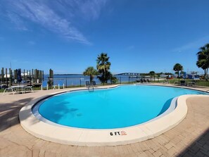 A clear blue swimming pool with a surrounding deck, a palm tree, and a view of the sea. - Sun Harbor Overlook - Sleeps 4 - 1 Bedroom Condo - Waterfront View (Panama City)