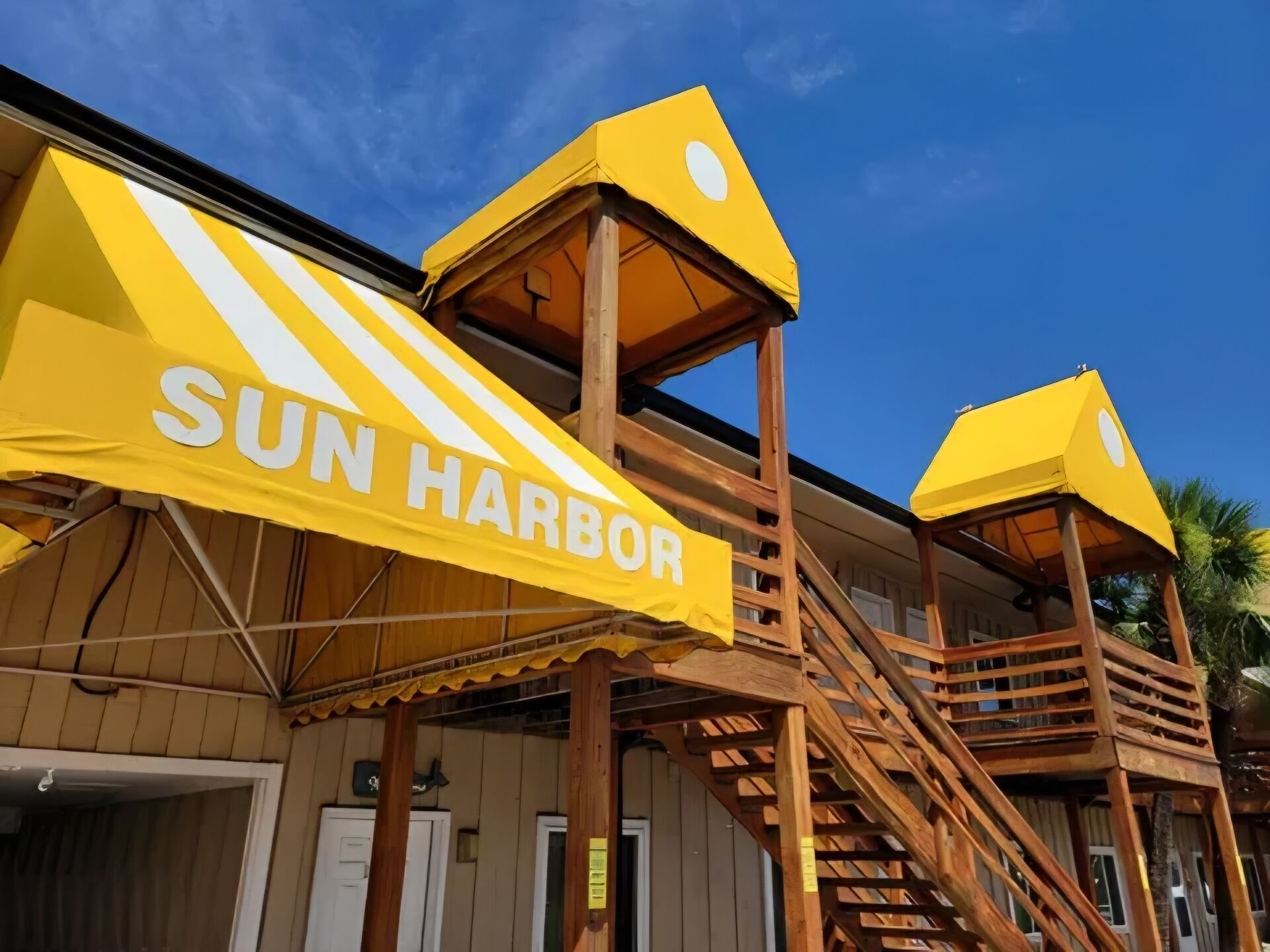 Un edificio con una escalera de madera y un amplio toldo amarillo que dice 'SUN HARBOR'.