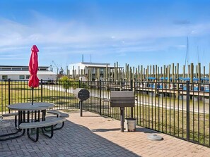 A picnic area with tables and benches, a barbecue grill, and a red umbrella. - Sun Harbor Overlook - Sleeps 4 - 1 Bedroom Condo - Waterfront View (Panama City)