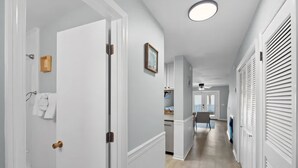 Un pasillo con puertas blancas, una lámpara en el techo y vista hacia un comedor.