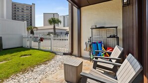 Un patio con cerca blanca, un pequeño jardín y una zona de estar con mesa y sillas.