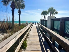A wooden boardwalk leading to a beach with palm trees and umbrellas. - Two Bed, Two Bath Townhouse | Sleeps 8 | Community Pool | No Additional Fees (Panama City)