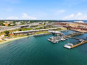 Un port de plaisance avec de nombreuses jetées et des bateaux, un grand bâtiment doté d’un toit plat, et une route avec un pont en arrière-plan.