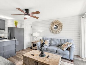 Un salon moderne avec un canapé gris, une table basse en bois et un ventilateur de plafond.