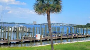 A waterfront marina with boats docked, a palm tree, and a bridge in the background. - Sun Harbor Serenity - Sleeps 4 - 1 Bedroom Condo Ground Floor Unit (Panama City)