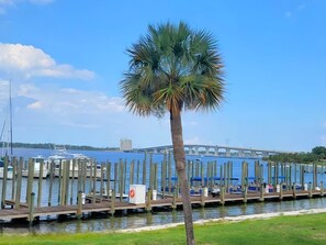 A waterfront marina with boats docked, a palm tree, and a bridge in the background. - Sun Harbor Serenity - Sleeps 4 - 1 Bedroom Condo Ground Floor Unit (Panama City)