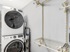 A laundry area with stacked washers and dryers, metal shelving units, and a wall-mounted rack. - Sun Harbor Serenity - Sleeps 4 - 1 Bedroom Condo Ground Floor Unit (Panama City)