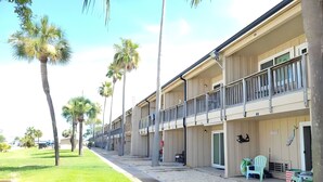 A row of two-story motel buildings with balconies, a grassy area, and palm trees. - Sun Harbor Serenity - Sleeps 4 - 1 Bedroom Condo Ground Floor Unit (Panama City)
