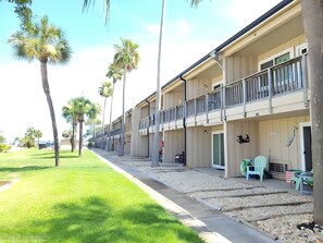 A row of two-story motel buildings with balconies, a grassy area, and palm trees. - Sun Harbor Serenity - Sleeps 4 - 1 Bedroom Condo Ground Floor Unit (Panama City)