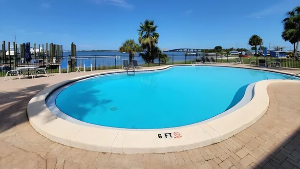 A clear blue swimming pool with a surrounding deck, a palm tree, and a view of the sea. - Sun Harbor Serenity - Sleeps 4 - 1 Bedroom Condo Ground Floor Unit (Panama City)
