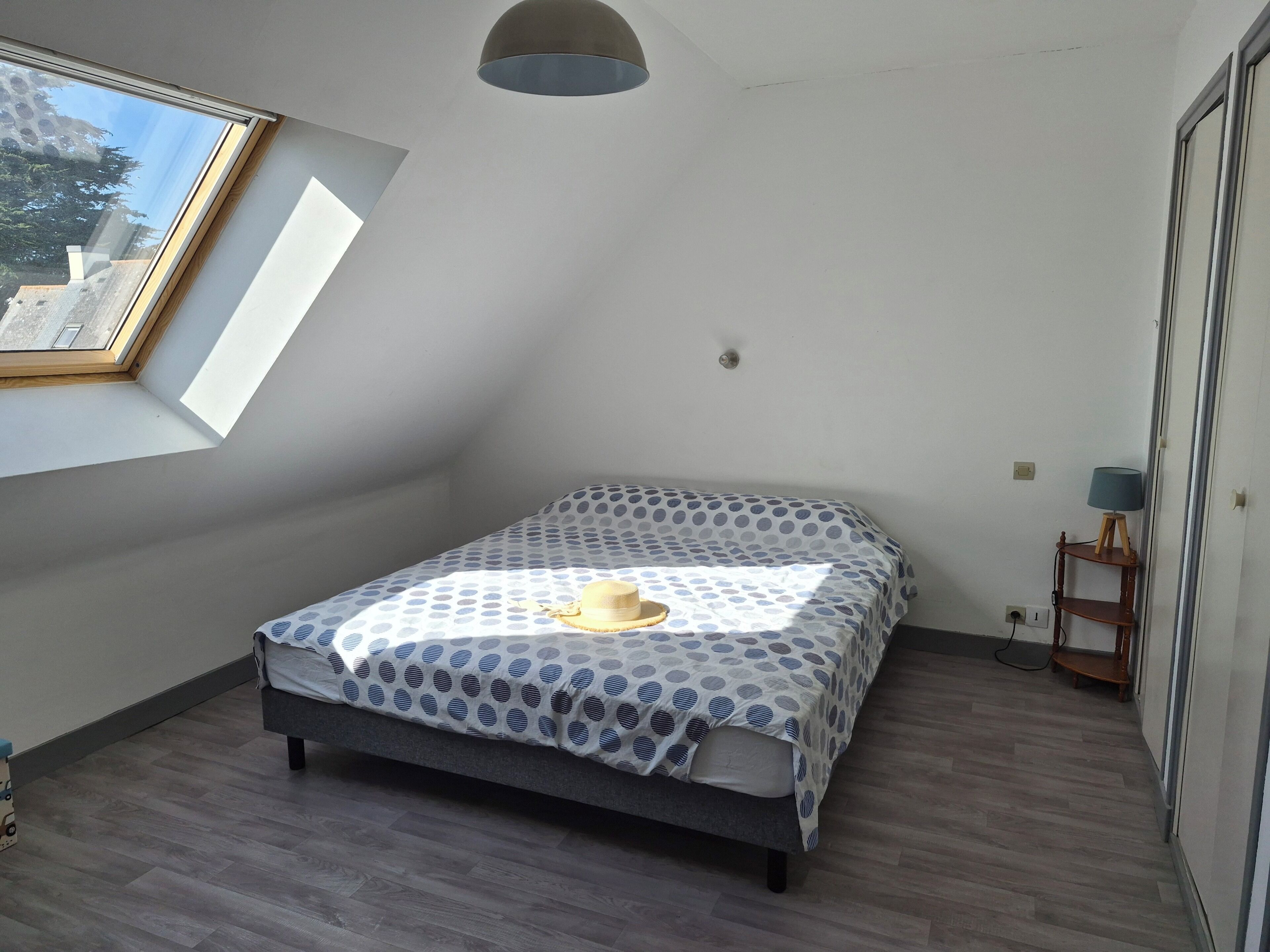 A bedroom with a bed, a skylight, a lamp, and a view of the outside.