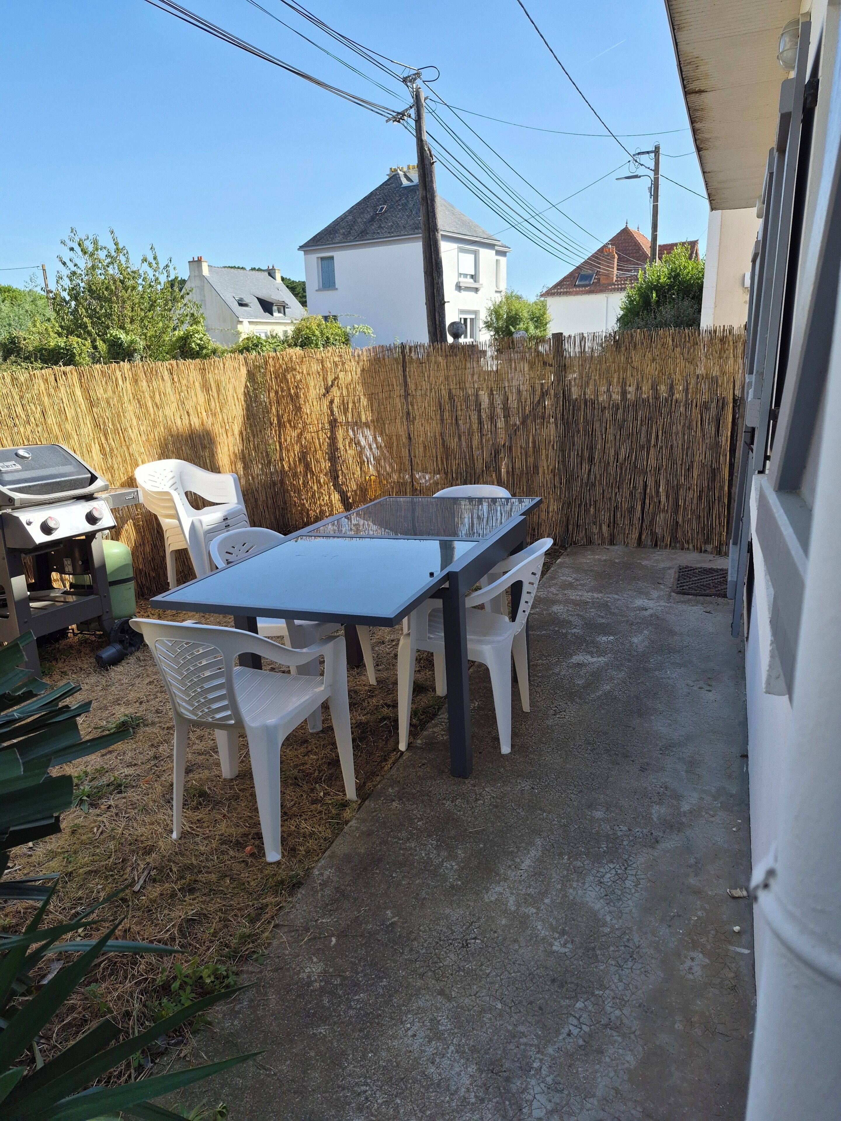 Een buitenterras met een tafel, stoelen, een barbecue en een hoge bamboescherm.